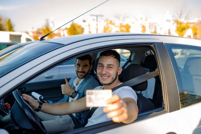 Jeune conducteur souriant au volant montrant son permis de conduire